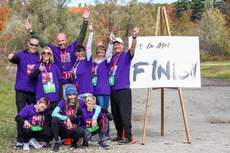 Participants celebrating with their medals beside the Art In Motion charity race finish line in Vaughan, Ontario